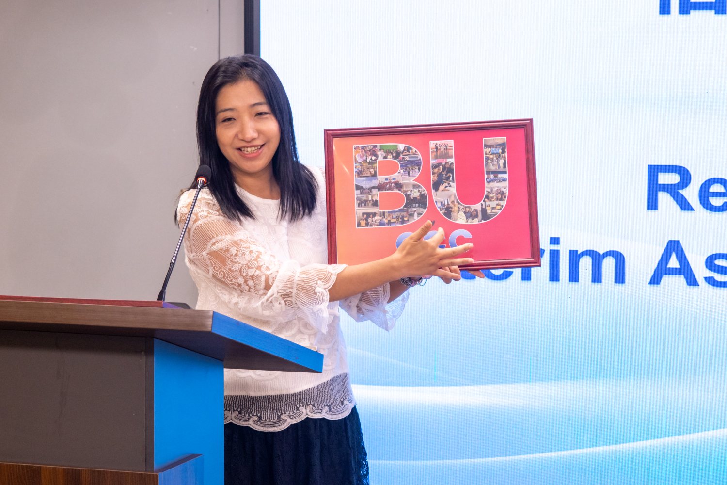Danni Liang 博士站在台上，手里捧着裱好的礼物。
